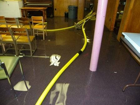 Standing water on a damaged floor with extraction hoses laid out for emergency response